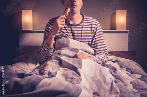 Photo: Young man is sitting in bed and eating chicken Young man is sitting in bed and eating chicken