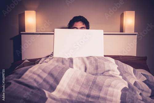 Photo: Man is sitting in bed behind his laptop Man is sitting in bed behind his laptop