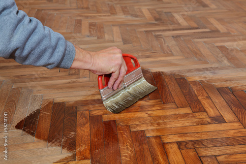 Photo: Varnishing of oak parquet floor, workers hand, brush, renovation Varnishing of oak parquet floor, workers hand, brush, renovation
