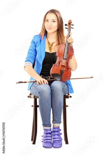 Photo: Casual young woman seated on a wooden chair holding a violin Casual young woman seated on a wooden chair holding a violin