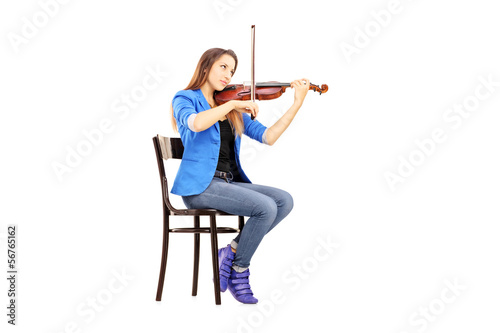 Photo: Casual young woman seated on a wooden chair playing the violin Casual young woman seated on a wooden chair playing the violin