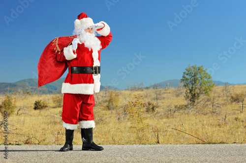 Photo: Santa claus holding a bag full of gifts on a road and looking Santa claus holding a bag full of gifts on a road and looking