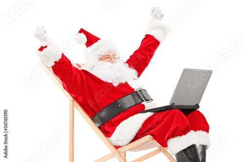 Photo: Santa Claus sitting on a chair with laptop gesturing happiness Santa Claus sitting on a chair with laptop gesturing happiness