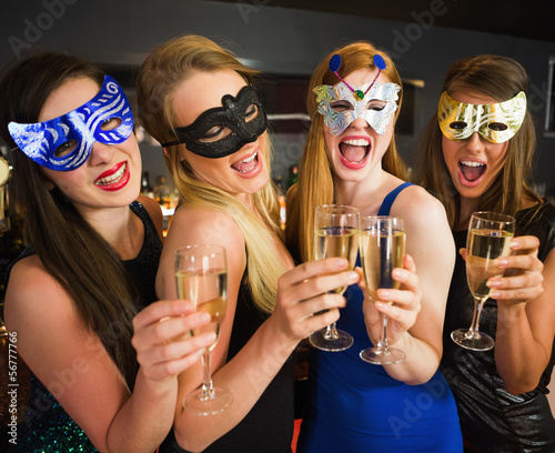 Photo: Attractive friends with masks on holding champagne glasses Attractive friends with masks on holding champagne glasses
