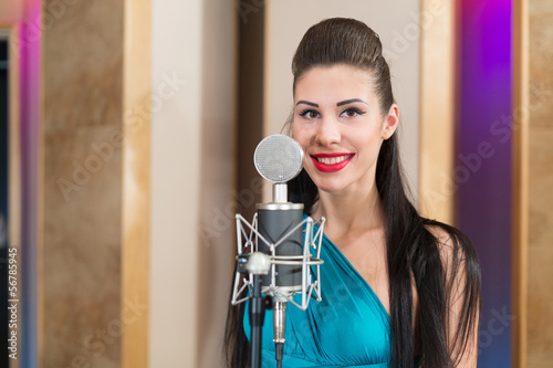 Photo: Smiling girl with red lips in room with microphone in Studio Smiling girl with red lips in room with microphone in Studio