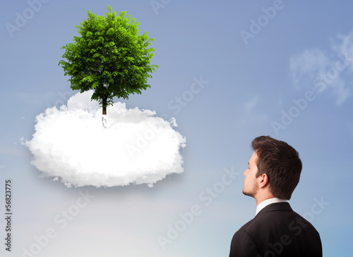 Photo: Young man pointing at a green tree on top of a white cloud Young man pointing at a green tree on top of a white cloud