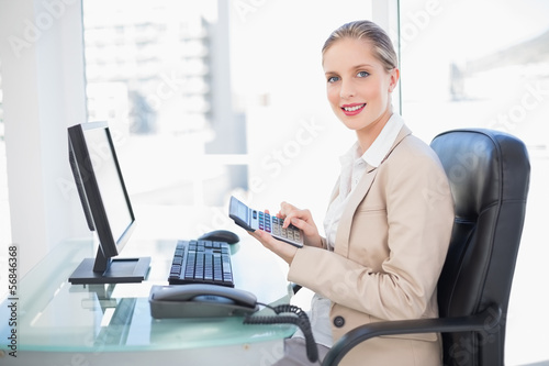 Photo: Side view of smiling blonde businesswoman using calculator Side view of smiling blonde businesswoman using calculator