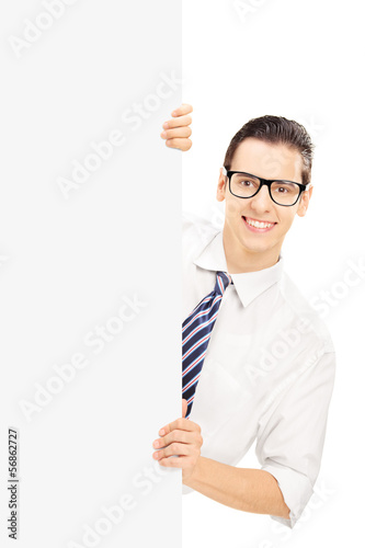 Photo: Young man with glasses posing behind a blank panel Young man with glasses posing behind a blank panel