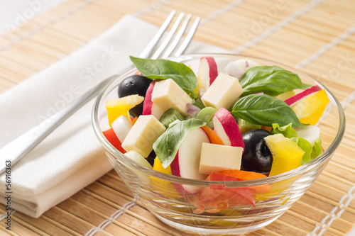 Photo: Fresh greek salad with fork on bamboo background Fresh greek salad with fork on bamboo background