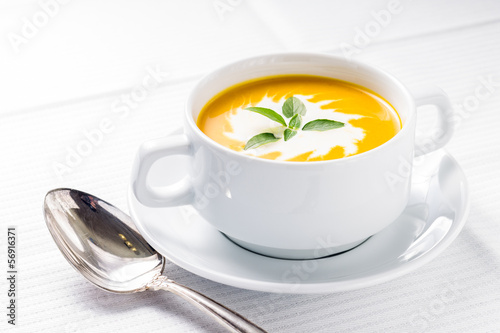 Photo: Pumpkin soup with basil on served table Pumpkin soup with basil on served table
