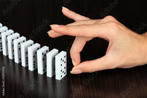 Photo: Hand pushing dominoes on wooden background Hand pushing dominoes on wooden background