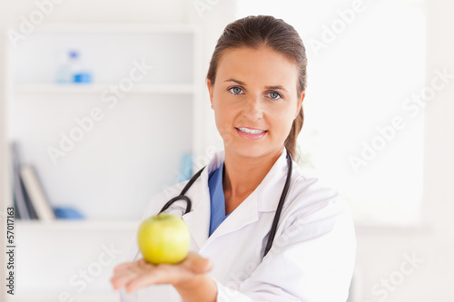Photo: Doctor with stethoscope holding an apple looking into the camera Doctor with stethoscope holding an apple looking into the camera