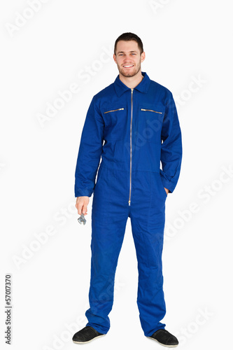 Photo: Smiling young mechanic in boiler suit holding a wrench Smiling young mechanic in boiler suit holding a wrench