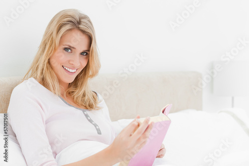 Photo: Side view woman holding a book and sitting in bed looking to the Side view woman holding a book and sitting in bed looking to the