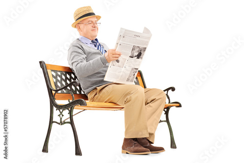 Photo: Senior gentleman reading newspaper and sitting on a bench Senior gentleman reading newspaper and sitting on a bench
