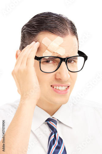 Photo: Serious young man with plaster on his forehead having a headache Serious young man with plaster on his forehead having a headache