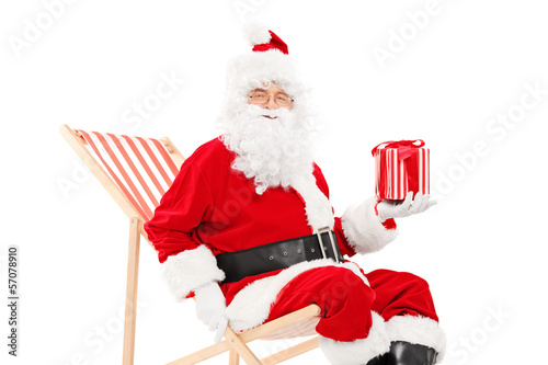 Photo: Smiling Santa Claus sitting on a beach chair and holding a gift Smiling Santa Claus sitting on a beach chair and holding a gift