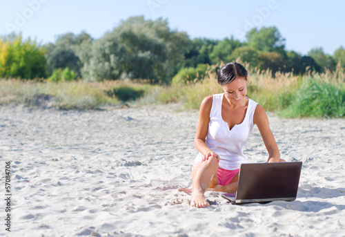 Photo: Attractive woman with laptop working on the beach Attractive woman with laptop working on the beach