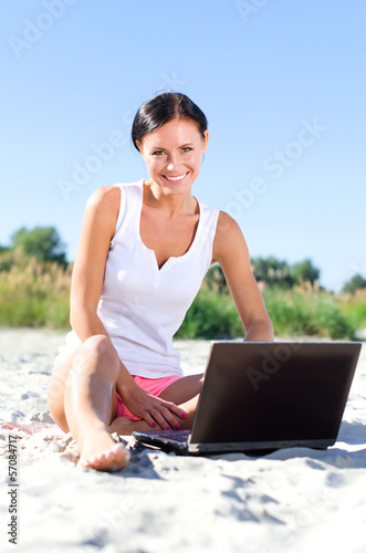Photo: Attractive woman with laptop working on the beach Attractive woman with laptop working on the beach