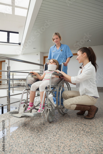 Photo: Mother crouching next to her child in wheelchair with nurse push Mother crouching next to her child in wheelchair with nurse push