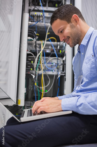 Photo: Man using laptop in front of servers Man using laptop in front of servers