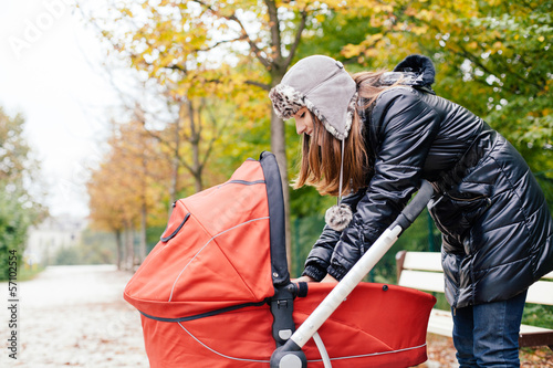 Photo: Young woman looking at her baby in stroller in a park Young woman looking at her baby in stroller in a park
