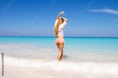 Photo: Young woman standing on a beach and enjoying the sun Young woman standing on a beach and enjoying the sun