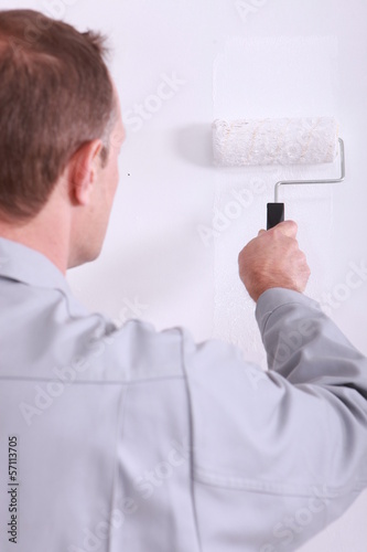Photo: Man painting a wall white with a roller Man painting a wall white with a roller