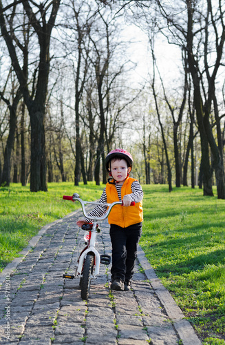Photo: Little boy pushing his bicycle in a park Little boy pushing his bicycle in a park