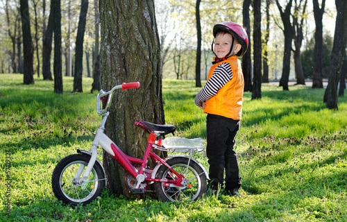 Photo: Little boy standing grinning alongside his bicycle Little boy standing grinning alongside his bicycle