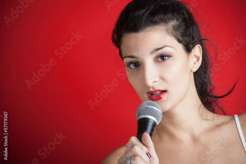 Photo: Beautiful girl singing with microphone against red background wi Beautiful girl singing with microphone against red background wi