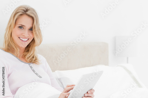 Photo: Woman in bed with tablet pc in hand looking up and smiling Woman in bed with tablet pc in hand looking up and smiling