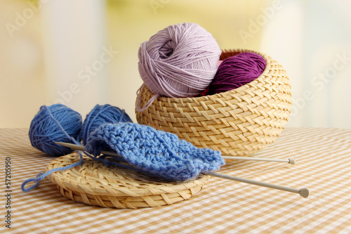 Photo: Multicolored clews in wicker basket with needles closeup Multicolored clews in wicker basket with needles closeup