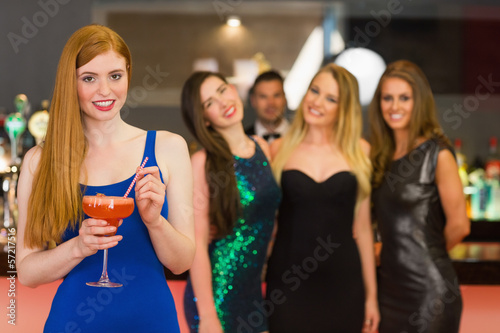 Photo: Attractive woman holding cocktail standing in front of her frien Attractive woman holding cocktail standing in front of her frien