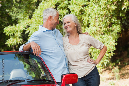 Photo: Smiling mature couple hugging by their red cabriolet Smiling mature couple hugging by their red cabriolet