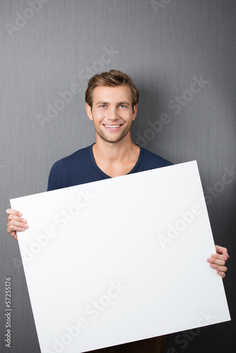 Photo: lächelnder junger mann zeigt weißes plakat lächelnder junger mann zeigt weißes plakat