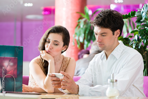 Photo: Young couple in cafe not interacting but on phone Young couple in cafe not interacting but on phone