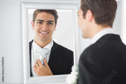 Photo: Cheerful young bridegroom standing in front of a mirror Cheerful young bridegroom standing in front of a mirror