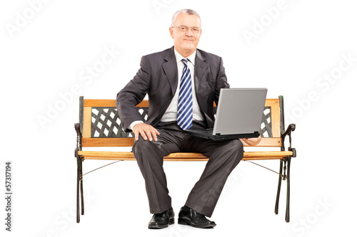 Photo: Mature professional man sitting on a bench working on laptop Mature professional man sitting on a bench working on laptop