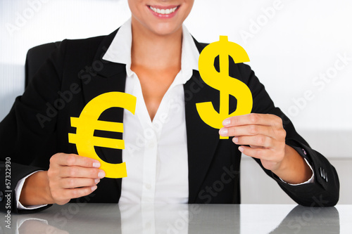 Photo: Businesswoman Holding Euro And Dollar Sign At Desk Businesswoman Holding Euro And Dollar Sign At Desk