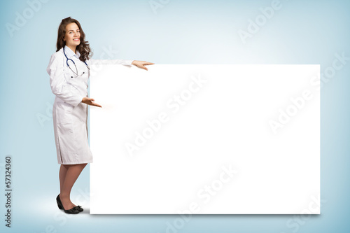 Photo: young woman doctor standing near a blank banner young woman doctor standing near a blank banner