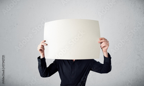 Photo: Businessman holding in front of his head a paper with copy space Businessman holding in front of his head a paper with copy space