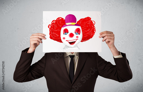 Photo: Businessman holding a cardboard with a clown on it in front of h Businessman holding a cardboard with a clown on it in front of h