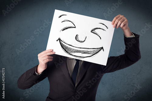 Photo: Businessman holding a paper with smiley face in front of his hea Businessman holding a paper with smiley face in front of his hea