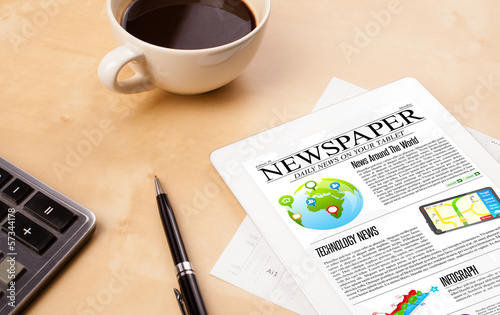 Photo: Tablet pc shows news on screen with a cup of coffee on a desk Tablet pc shows news on screen with a cup of coffee on a desk