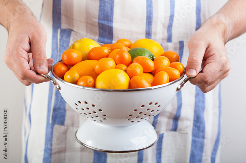 Photo: man hands holding colander with citrus fruits man hands holding colander with citrus fruits