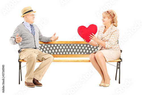 Photo: Mature female giving a red heart to a surprised man, on a bench Mature female giving a red heart to a surprised man, on a bench