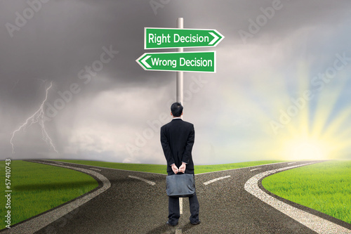Photo: Businessman looking at sign of right vs wrong decision Businessman looking at sign of right vs wrong decision
