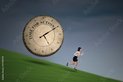 Photo: Businesswoman running with a big time clock on hill Businesswoman running with a big time clock on hill