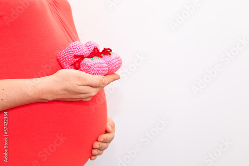 Photo: Pregnant woman holding pink baby shoes on her belly Pregnant woman holding pink baby shoes on her belly